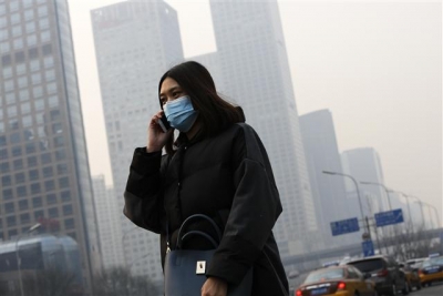 ▲7일(현지시간) 중국 수도 베이징 시 당국이 사상 처음으로 스모그 적색 경보를 발령했다. 사진은 이날 한 여성이 마스크를 쓴채 베이징 시내를 지나가는 모습. AP뉴시스