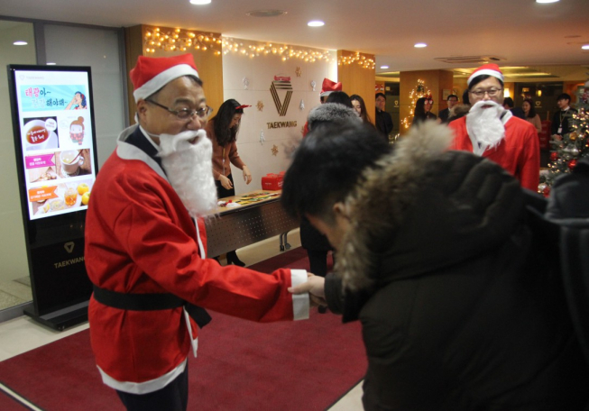 ▲지난 20일 서울 중구 장충동 사옥에서 진행한 태광산업 크리스마스 행사에서 산타복장을 한 홍현민 대표이사(왼쪽)가 출근하는 직원에게 인사를 건네고 있다.(사진제공=태광산업)