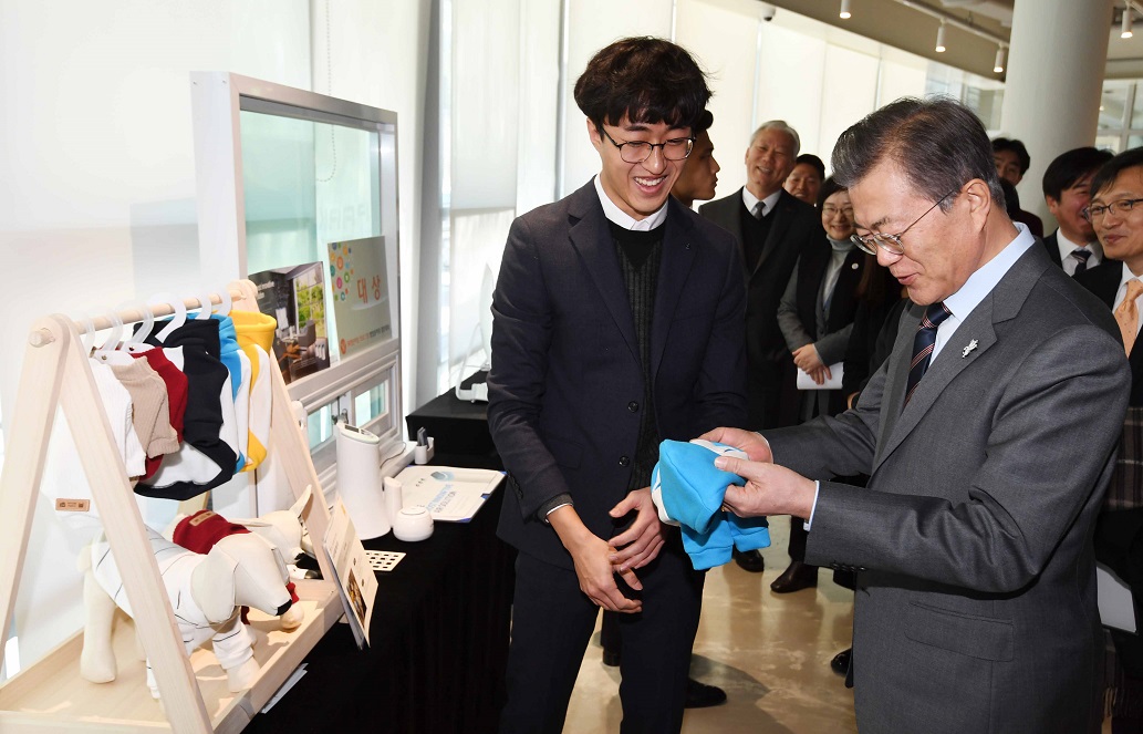 ▲문재인 대통령이 12일 울산시 울주군 울산과학기술원(UNIST)를 방문해 헌 옷을 업사이클링해 반려동물 용품을 판매하는 '미싱피플' 제품을 살펴 본 후 반려견 토리의 옷을 선물받고 있다.(뉴시스)