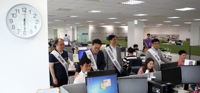 ▲롯데자산개발 임원들이 정시퇴근을 독려하는 캠페인을 진행하고 있다. 이광영 대표이사(왼쪽에서 3번째)가 직접 사무실을 다니며 정시퇴근을 권유하고 있다. 컴퓨터 화면에는 정시퇴근 시간을 알리는 팝업창이 떠있다.(사진제공=롯데자산개발)