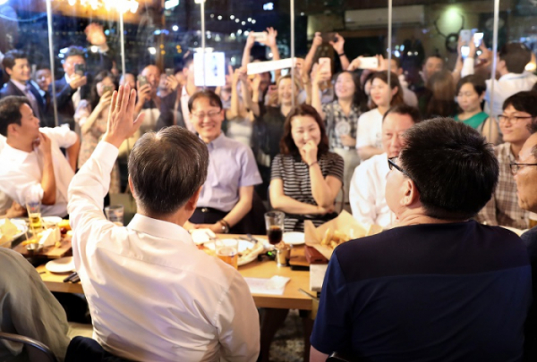 ▲문재인 대통령이 26일 오후 서울 광화문 인근 한 맥줏집에서 퇴근길 시민들과 만나 호프타임을 갖는 동안 시민들이 몰려 지켜보자 손을 들어 인사하고 있다.(연합뉴스)