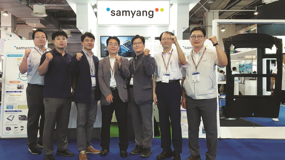 ▲삼양사 조성환 화학연구소장(우측에서 세번째)이 상해 복합소재 전시회에서 C-LFT로 만든 자동차 선루프 프레임(사진 가장 우측)을 내세운 전시 부스를 배경으로 기념촬영을 하고 있다. (사진제공=삼양사)