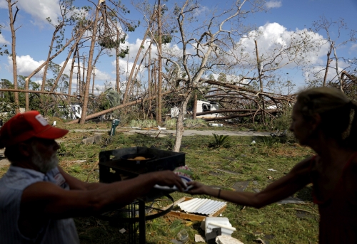 ▲11일(현지시간) 미국 플로리다 캘러웨이에 불어닥친 열대성 폭풍 마이클로 파괴된 집 안 뜰에서 주민 두명이 음식을 먹고 있다. 캘러웨이/AP연합뉴스
