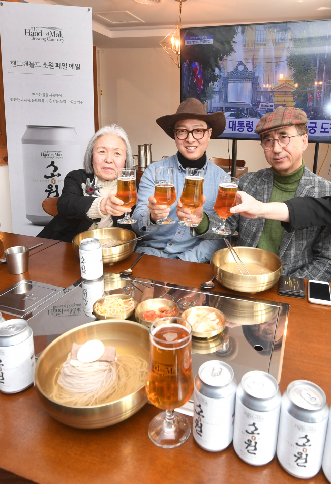 ▲2차 북미정상회담이 개최되는 27일, 서울 서초구에 위치한 ‘동무밥상’ 서초점에서 핸드앤몰트가 실향민들과 최근 출시된 ‘소원 페일 에일’을 시음하는 자리를 가졌다. 실향민 오승희 동덕여대 명예교수와 핸드앤몰트 도정한 설립자, 이북오도위원회 이혁진 사무국장이 남북 화합을 염원하는 축배를 들고 있다.