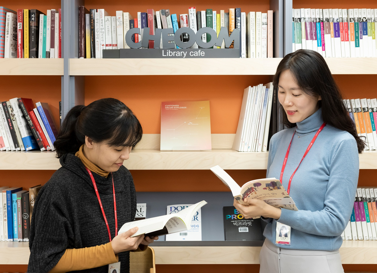 ▲ SK네트웍스의 라이브러리 카페 ‘채움’이 봄맞이 새 단장을 마치고 구성원들의 채움 도우미로 나섰다. SK네트웍스 구성원들이 새롭게 구성된 ‘사회적 가치’ 코너 앞에서 책을 읽고 있다.(사진 제공=SK네트웍스)