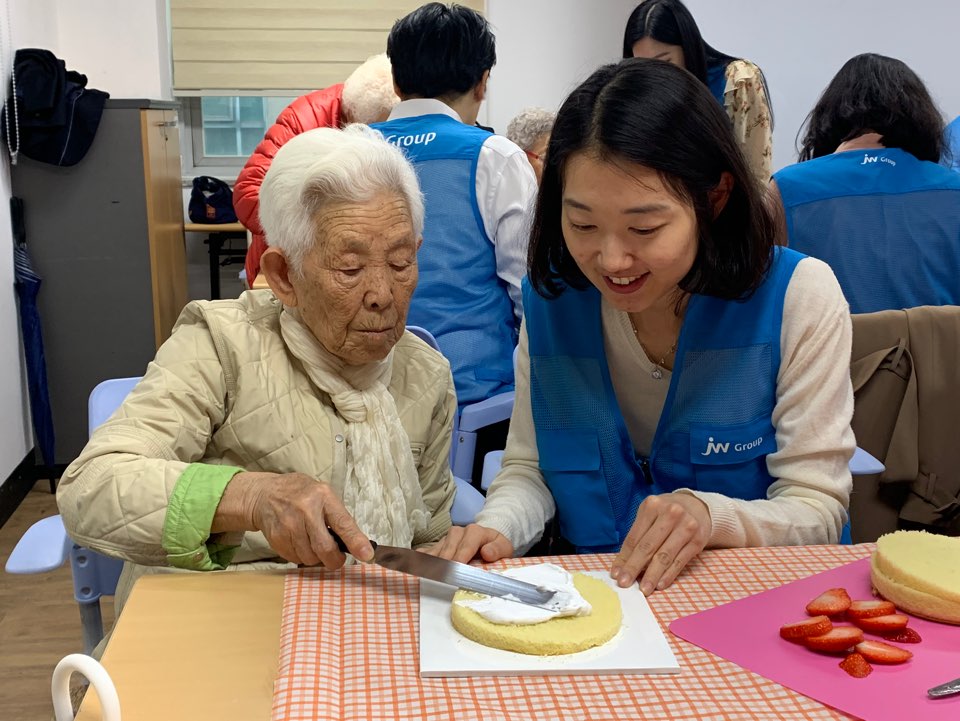▲JW한마음봉사단원이 어르신과 짝을 이뤄 케이크를 만들고 있다.(사진제공=JW그룹)