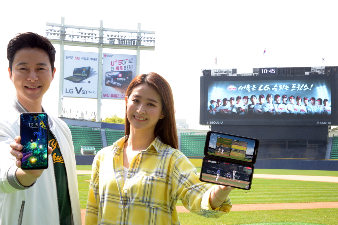 ▲G전자가 지난 10일 국내 출시한 5G 스마트폰 LG V50 ThinQ를 알리기 위한 마케팅 활동에 가속도를 낸다. LG전자 모델들이 서울 송파구 소재 잠실야구장 외야 조명탑에 설치된 옥외광고를 배경으로 LG V50 씽큐를 소개하고 있다.(사진제공=LG전자)
