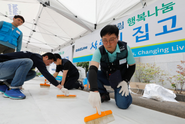 ▲박상신 대림산업 대표(우측 첫번째)가 도배작업에 사용할 벽지에 풀칠을 하고 있다.(사진=대림산업)