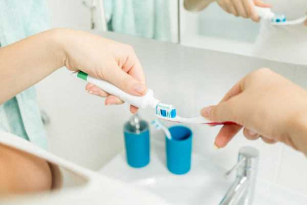 ▲Closeup image of woman putting toothpaste on toothbrush in cup at bathroom