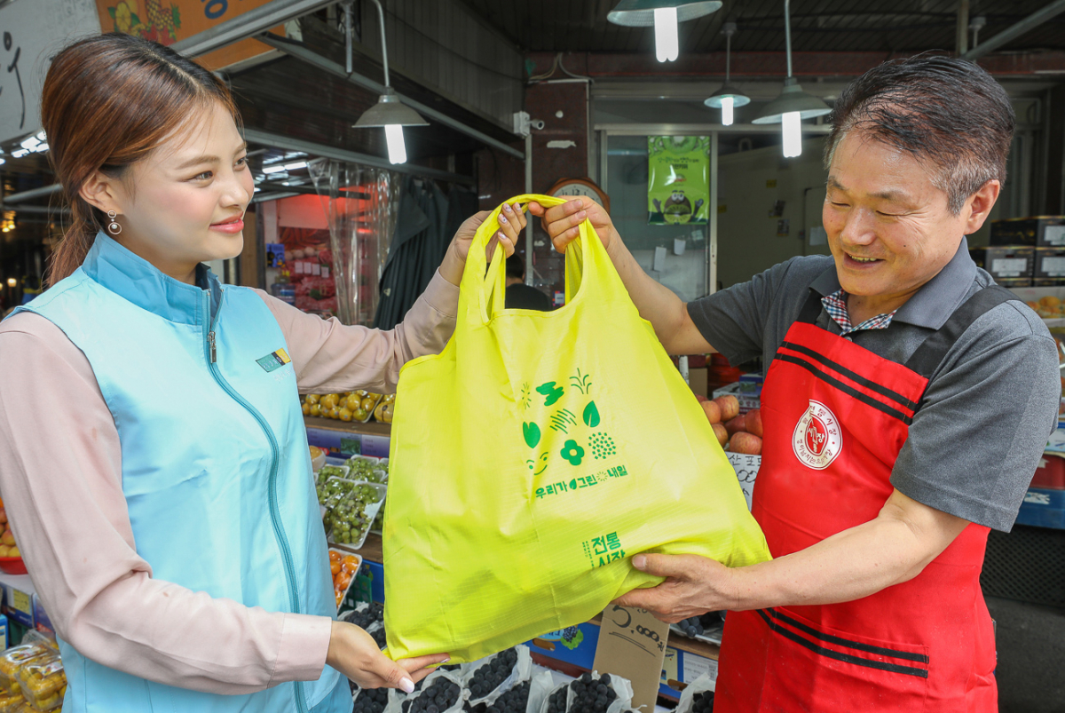 ▲8일 현대백화점 직원이 서울 양천구 목사랑시장 내 상인에게 '우리가 그린 내일' 장바구니를 전달하고 있는 모습. (사진제공=현대백화점)
