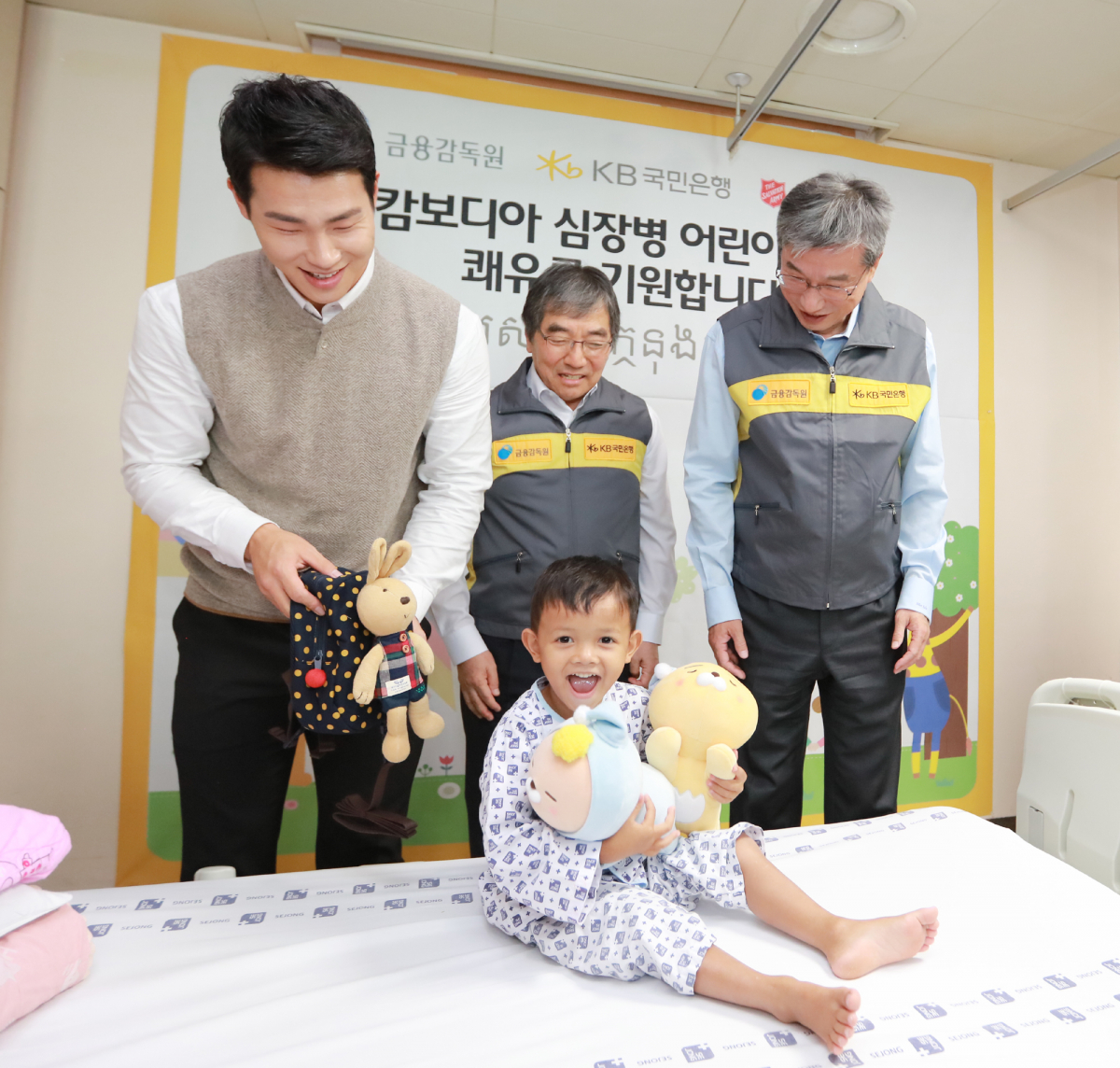 ▲(왼쪽부터)윤성빈 KB금융 후원선수와 윤석헌 금융감독원장, 허인 KB국민은행장이 19일 경기도 부천 세종병원을 방문해 국내에서 심장병 수술을 마치고 회복 중인 캄보디아 어린이에게 선물을 주고 있다.(KB국민은행)