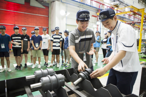 ▲‘Doosan Tomorrow Lab(두산과학교실)’에 참가하는 학생들이 지난해 8월 두산인프라코어 인천공장을 견학하며 건설기계 부품을 직접 만져보는 모습.  (사진제공=두산)