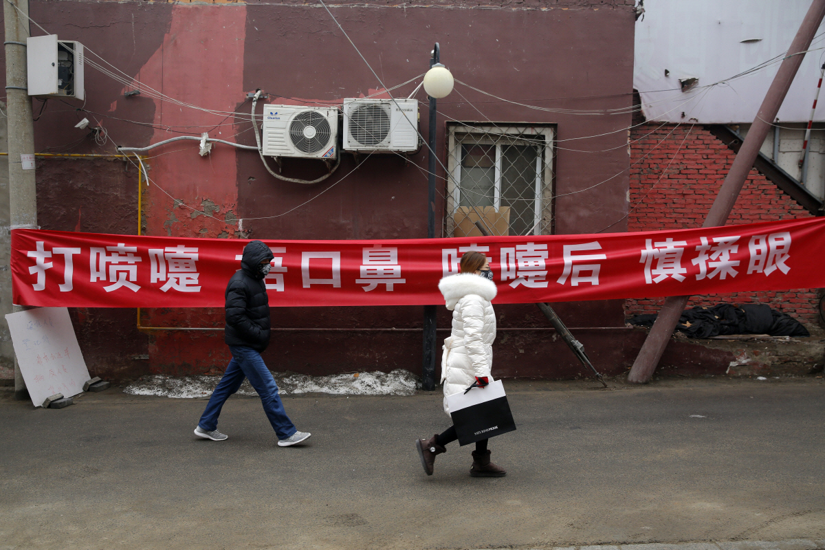 ▲중국 베이징의 한 골목에서 13일(현지시간) 행인들이 마스크를 쓰고 ‘기침을 할 때 코와 입을 가리고 기침 후에는 눈을 만지지 마시오’라고 적힌 현수막 앞을 걸어가고 있다. 베이징/EPA연합뉴스