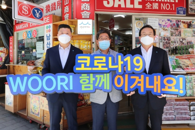 ▲손태승 우리금융그룹 회장(사진 오른쪽)과 권광석 우리은행장(사진 왼쪽)이 서울 중구에 위치한 남대문시장에서 물품을 구매한 뒤 박칠복 남대문시장 남산상회 대표(가운데)와 코로나19 극복을 다짐하며 기념촬영을 하고 있다.