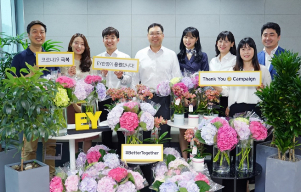 ▲EY한영 ’땡큐 스마일 캠페인(Thank you Smile Campaign)’을 통해 동료로부터 꽃을 선물 받은 EY한영 임직원들이 박용근 대표이사(왼쪽 넷째)와 함께 코로나19 극복의 메시지를 담은 플래카드를 들고 기념촬영을 하고 있다.  (사진제공=EY한영)