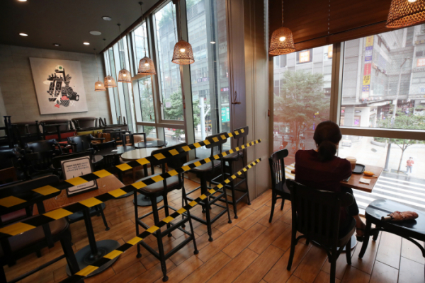 ▲사회적 거리두기 2단계 조치 중인 서울의 한 카페의 이용객 곁에 사용하지 않는 테이블과 의자가 쌓여있다. (연합뉴스)