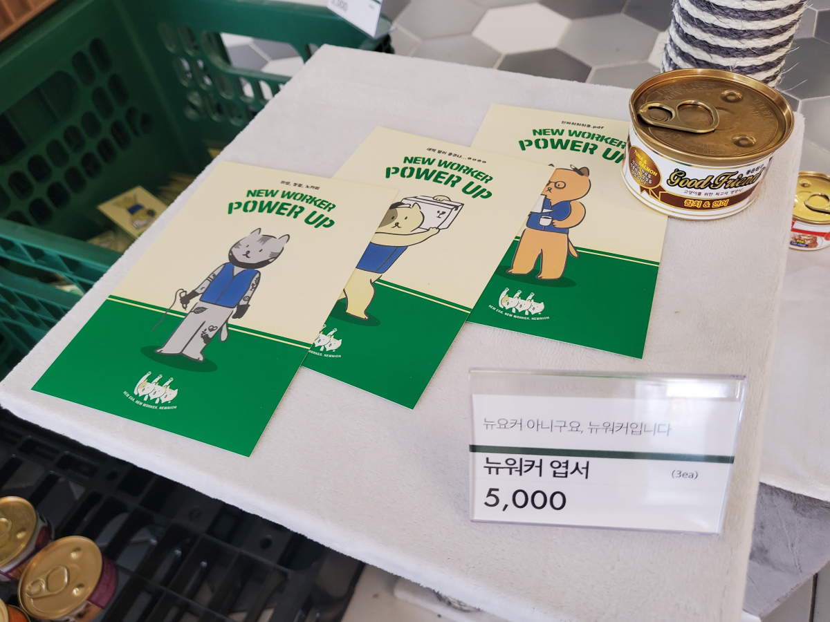 ▲‘뉴워커 프로젝트: 파워업스토어’에 고양이 캔과 함께 놓인 ‘뉴워커 프로젝트’ 엽서. 고양이들은 각각 타투이스트, 디자이너, 배달노동자를 상징한다.  (안유리 수습기자 inglass@)