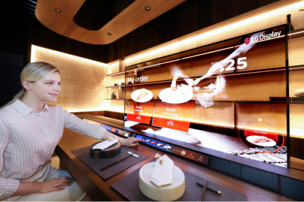 ▲LG디스플레이가 CES2021에서 선보이는 '레스토랑존'에서 모델이 투명 OLED를 이용해 메뉴를 살펴보고 있다.  (사진제공=LG디스플레이)