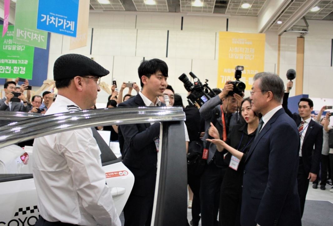 ▲문재인 대통령이 2019년 7월 5~7일 대전컨벤션센터·대전무역전시관에서 열린 제2회 대한민국 사회적경제 박람회장에서 '고요한 택시' 송민표 대표로부터 설명을 듣고 있다. 고요한 택시는 청각장애인들이 택시기사 직업을 가질 수 있도록 돕고 있다. (사진제공=한국사회적기업진흥원)