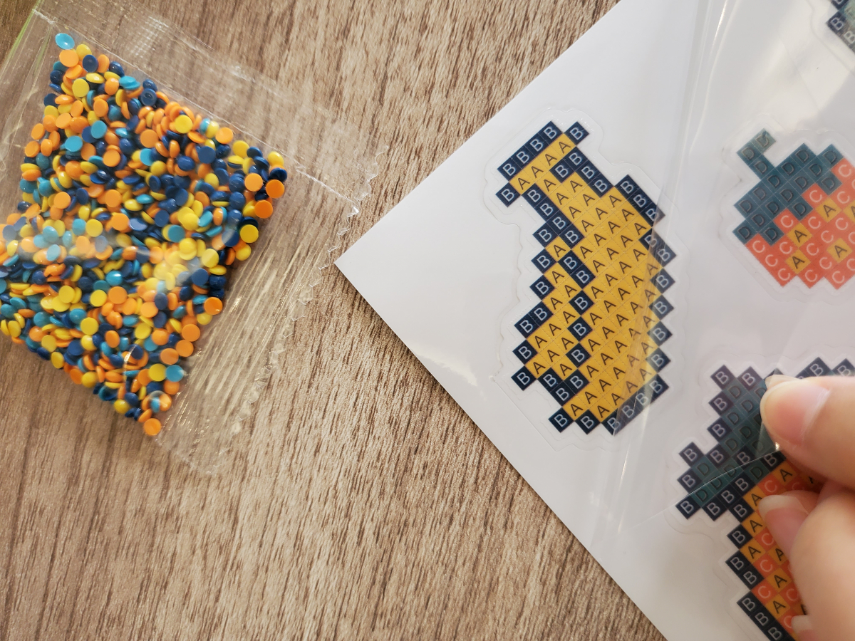 ▲보석 십자수의 도안 표면에는 접착면을 보호하기 위한 ‘보호 필름’이 붙여져 있다. 보호 필름의 접착액이 날아가면 보석을 다시 붙이기 어려워 작업을 하지 않을 때엔 반드시 보호 필름을 다시 붙여 놓아야 한다. (사진=안유리 기자 inglass@)