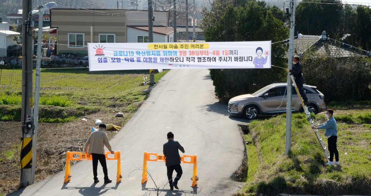▲전북 전주시 덕진구 호성동 한사월마을의 코로나19 확진자가 급속도로 늘어나고 있는 30일 한사월마을에서 관계자들이 이동제한 조치를 알리는 현수막을 붙이고 입구를 통제하고 있다. (뉴시스)