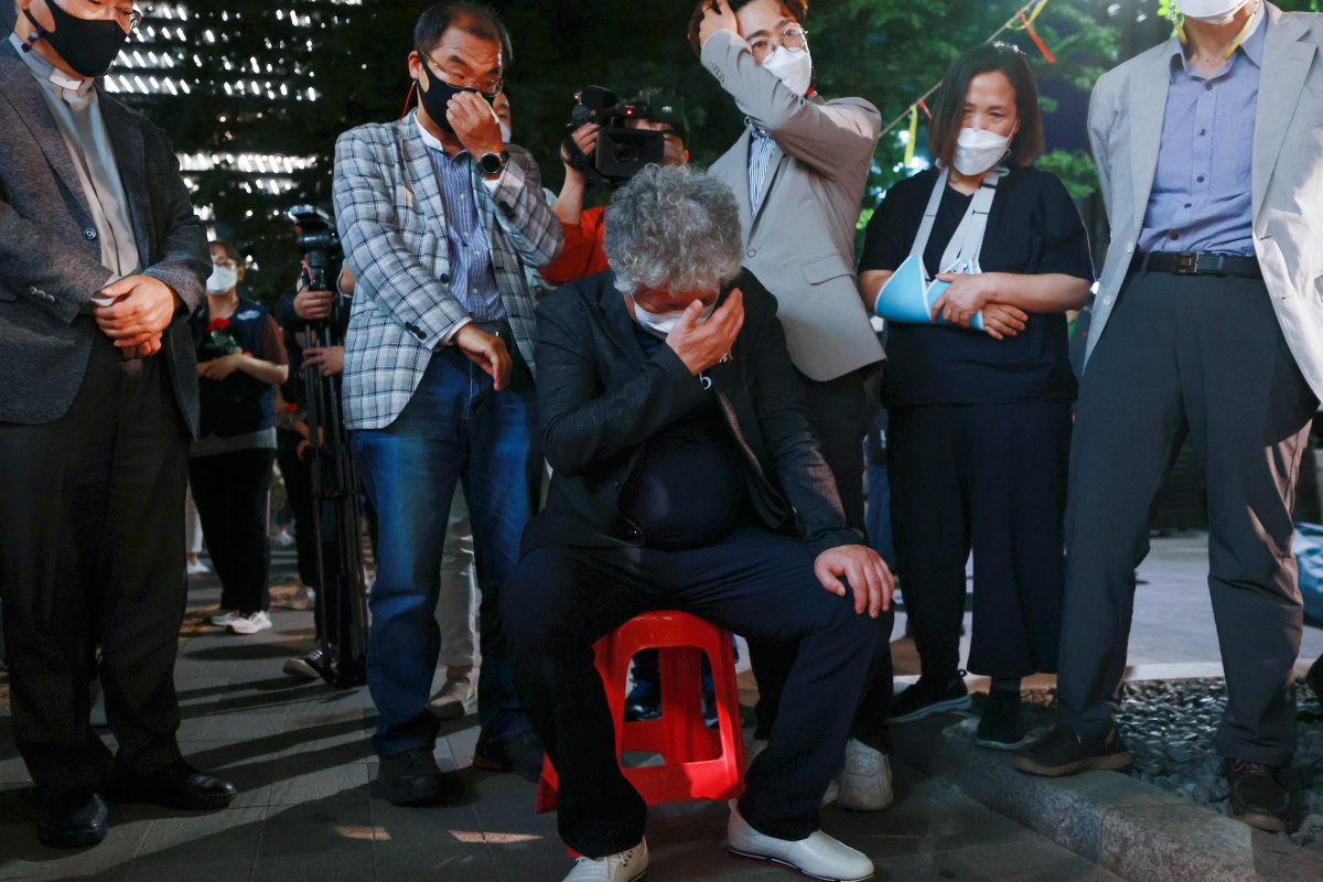 ▲평택항에서 일하다 사고로 숨진 20대 청년 노동자 고(故) 이선호 씨의 부친 이재훈 씨가 13일 오후 서울 중구 서울지방고용청 앞에서 열린 추모문화제에서 아들의 얼굴이 새겨진 현수막을 바라보던 중 의자에 앉아 눈물을 흘리고 있다.  (연합뉴스)