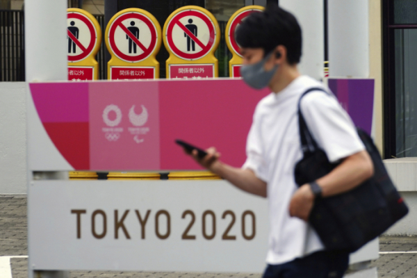 ▲한 남성이 11일(현지시간) 마스크를 쓴 채 도쿄 시내에 있는 도쿄올림픽 배너 앞을 지나가고 있다. 도쿄/AP뉴시스 