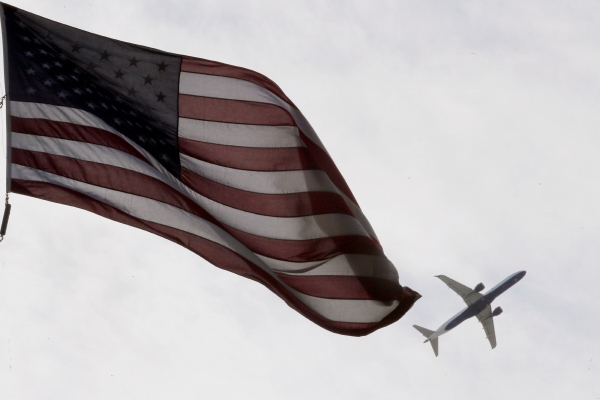 ▲27일(현지시간) 미국 매사추세츠주 보스턴에서 미국 국기 뒤로 비행기 한 대가 날아가고 있다. 보스턴/로이터연합뉴스
