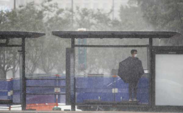 ▲23일 서울 종로구 광화문네거리 인근 버스정류장에서 갑자기 내린 소나기에 시민이 비를 피하고 있다.  (뉴시스)