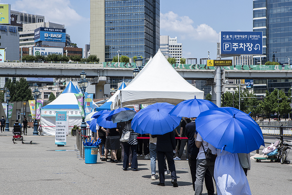 ▲폭염이 기승을 부린 16일 서울 중구 서울역 광장 선별진료소에서 시민들이 양산을 쓰고 검사를 기다리고 있다.  (연합뉴스)
