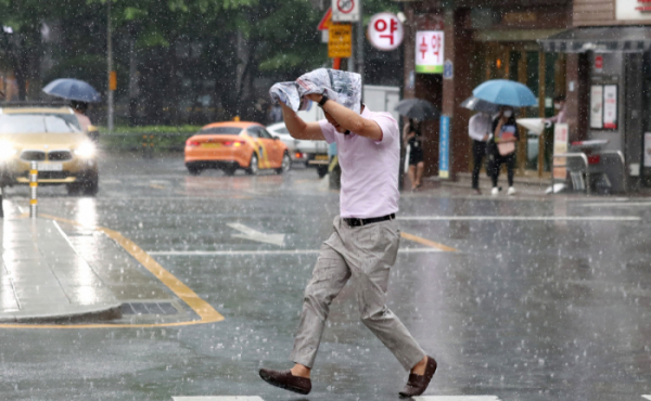 ▲지난달 30일 서울 종로구 세종문화회관 일대에서 한 시민이 신문을 머리에 쓰고 비를 피하고 있다. (뉴시스)
