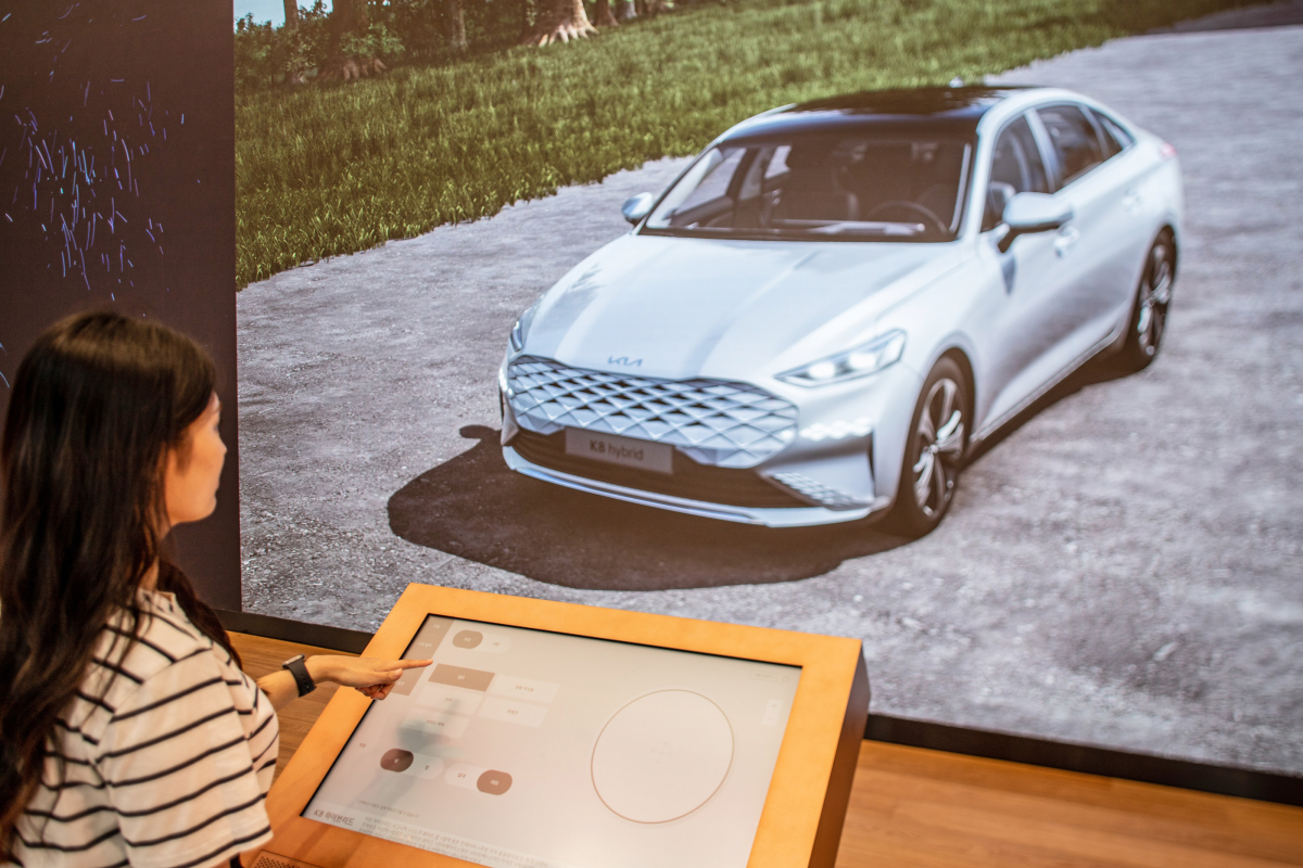 ▲강서 플래그십 스토어에 설치된 대형 미디어 월과 그 앞에서 ‘3D 컨피규레이터’를 통해 차량을 3D 이미지로 체험하고 있다. (사진제공=기아)