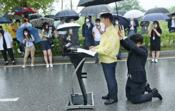 ▲강성국 법무부 차관이 27일 오후 충북혁신도시 국가공무원인재개발원 정문 앞에서 아프가니스탄 특별기여자 초기 정착 지원을 발표하는 브리핑을 하는 동안 한 직원이 뒤쪽에 무릎을 꿇고 우산을 받쳐주고 있다.  (뉴시스)