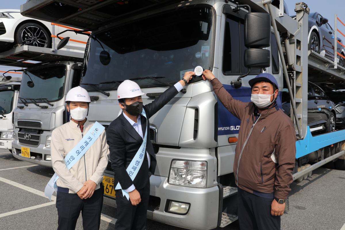 ▲(왼쪽부터) 현대글로비스 국내물류사업부 김보성 상무, 한국교통안전공단 검사전략실 오태석 실장, 현대글로비스 위수탁 차주 박국만 기사가 4일 현대글로비스 충주사무소에서 ‘카캐리어 안전운행 캠페인’의 일환으로 작업자 추락방지 안전난간대를 설치한 자동차운반트럭에 인증 스티커를 부착하고 있다. (사진제공=현대글로비스)