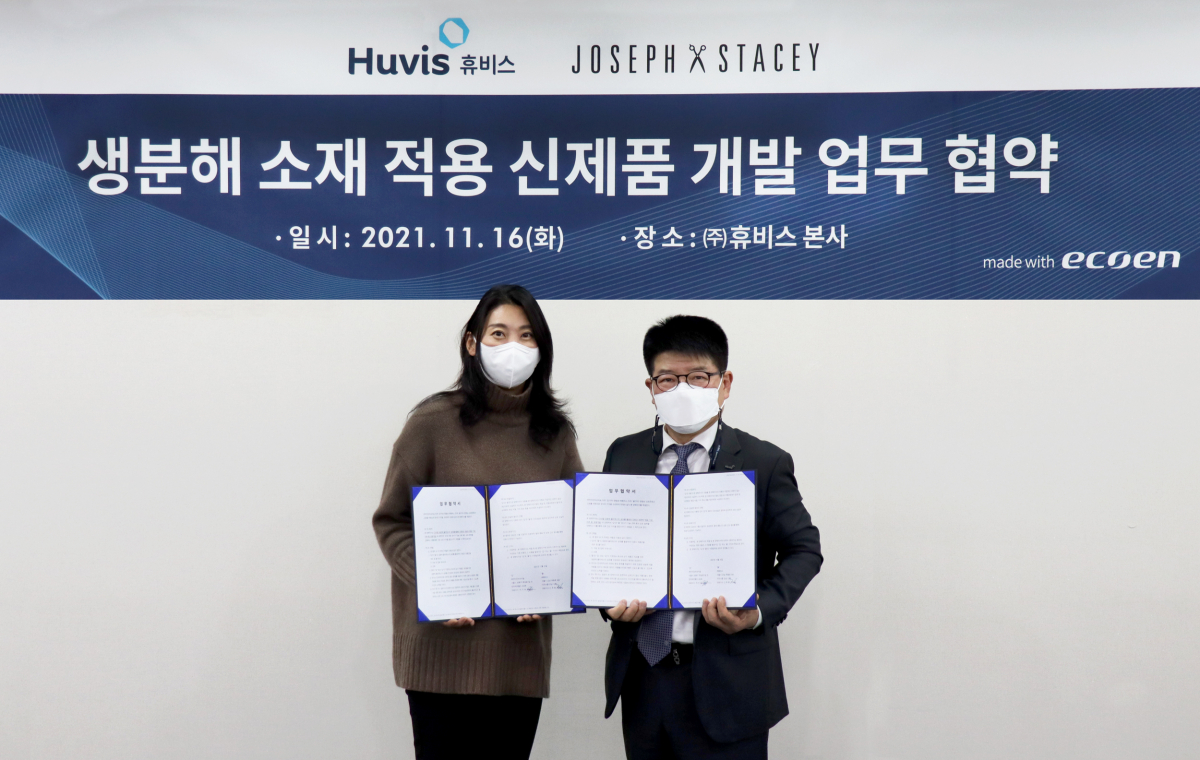 ▲김봉섭(오른쪽) 휴비스 Yarn 사업본부장과 허지숙 마치인터내셔널 대표가 업무 협약을 맺은 뒤 생분해 섬유 에코엔으로 만들어진 현수막 앞에서 기념사진을 찍고 있다. (사진제공=휴비스)