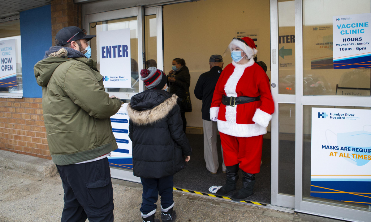 ▲캐나다 토론토에서 한 여성이 25일(현지시간) 신종 코로나바이러스 감염증(코로나19) 백신 접종 센터 앞에서 산타 복장을 한 채 어린이를 반기고 있다. 토론토/AP뉴시스