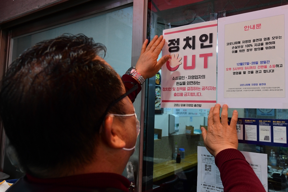 ▲22일 서울 시내의 한 식당가에서 코로나피해자총연합회 회원이 '정치인 출입 금지' 안내문을 붙이고 있다.  (조현호 기자 hyunho@)