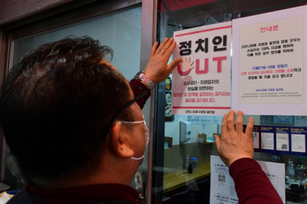 ▲22일 서울 시내의 한 식당가에서 코로나피해자총연합회 회원이 '정치인 출입 금지' 안내문을 붙이고 있다.  (조현호 기자 hyunho@)