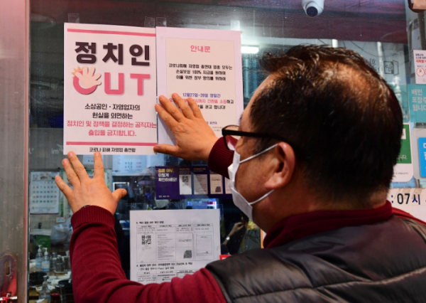 ▲22일 서울 시내의 한 식당가에서 코로나피해자총연합 회원이 '정치인 출입 금지' 안내문을 붙이고 있다. 조현호 기자 hyunho@ (이투데이DB)