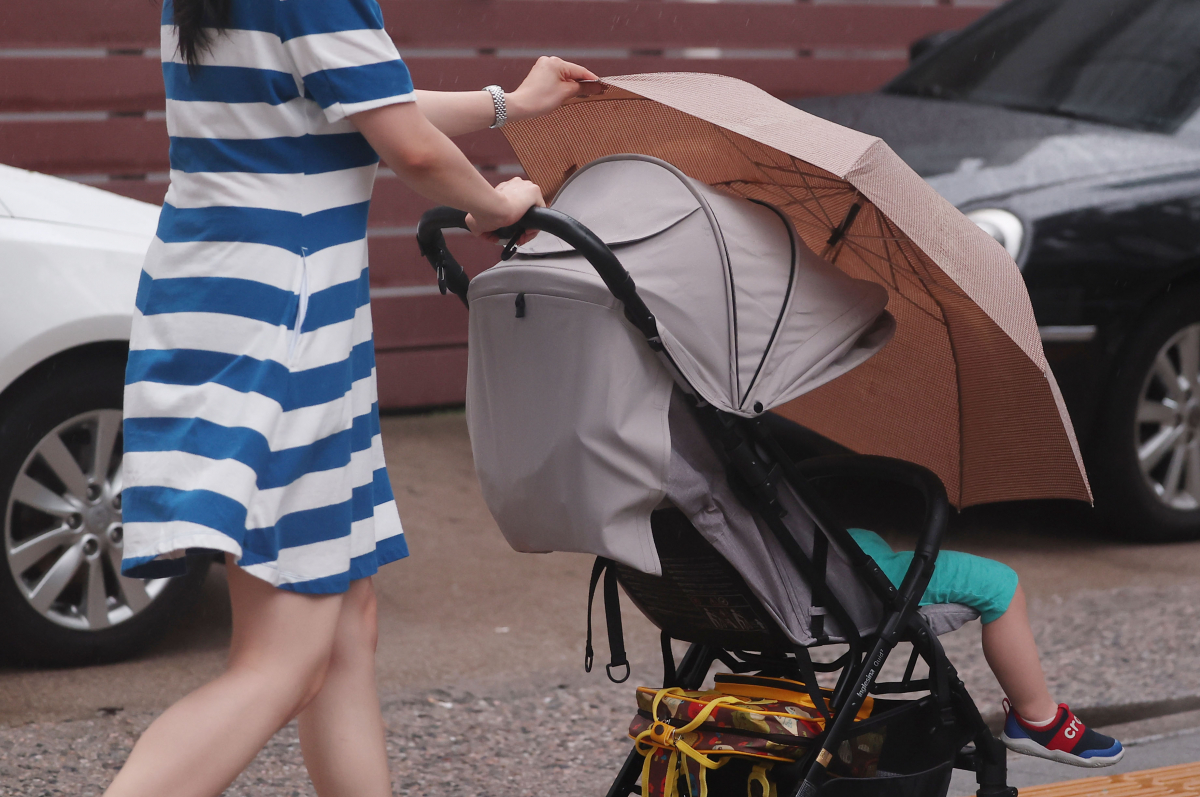 ▲29일 오후 서울 충정로를 지나던 한 시민이 비가 내리자 우산을 아이에게 씌워주고 있다. (연합뉴스)