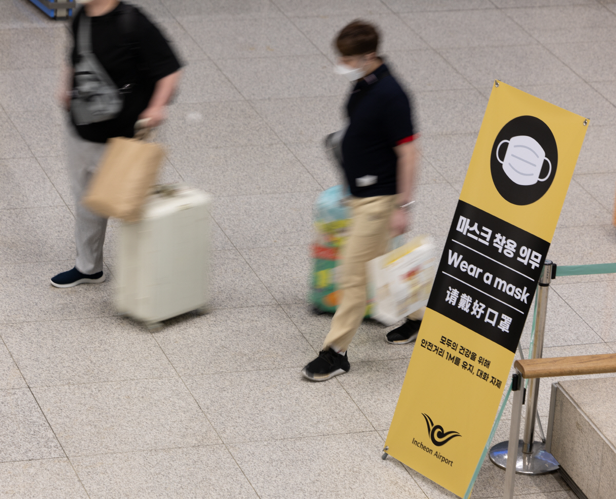 ▲국내에 도착하는 내·외국인에 대해 코로나19 음성 확인서 제출 의무가 해제된 뒤 맞은 첫 휴일인 4일 오후 인천공항을 통해 입국한 여행객들이 마스크 착용과 입국 뒤 코로나19 검사소 위치 안내가 담긴 홍보물 앞을 지나가고 있다.(연합뉴스)
