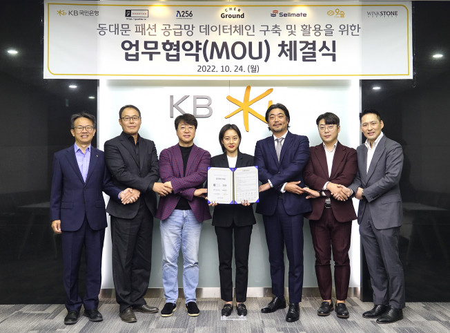 ▲지난 24일 서울시 영등포구 KB국민은행 여의도 IT센터에서 열린 동대문 패션 공급망 데이터체인 구축 및 활용을 위한 업무협약식에서 (왼쪽부터) 윤진수 KB국민은행 테크그룹 대표, 이한수 굿티어 대표, 박재현 람다256 대표, 이연 쉐어그라운드 대표, 서원준 셀메이트 대표, 조형일 위아더 대표, 권오형 윙크스톤파트너스 대표가 기념촬영을 하고 있다.