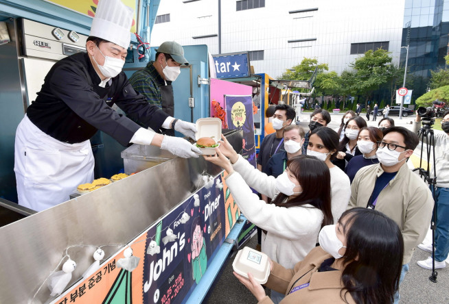 ▲존림 삼성바이오로직스 대표가 4공장 가동 기념으로 열린 푸드트럭 행사에서 셰프 복장으로 임직원들에게 햄버거와 수제맥주를 나눠주고 있다. (사진제공=삼성바이오로직스)