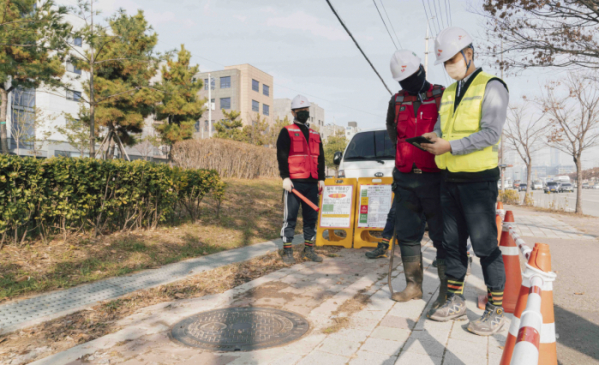▲SK텔레콤과 SK오앤에스 작업자들이 IoT 센서로 측정한 맨홀 내부 정보를 스마트폰으로 확인하는 작업을 진행하고 있다.  (사진제공=SK텔레콤)