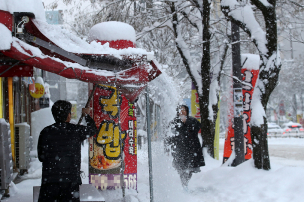 ▲지난달 23일 광주 북구 용두동에서 한 시민이 상점의 그늘막에 쌓인 눈을 털어내고 있다.  (연합뉴스)