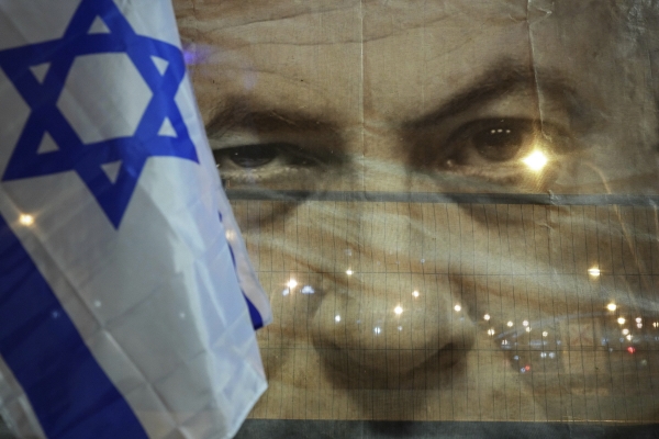 ▲이스라엘 국기 너머로 21일 베냐민 네타냐후 총리 얼굴이 그려진 현수막이 보인다. 텔아비브/AP뉴시스
