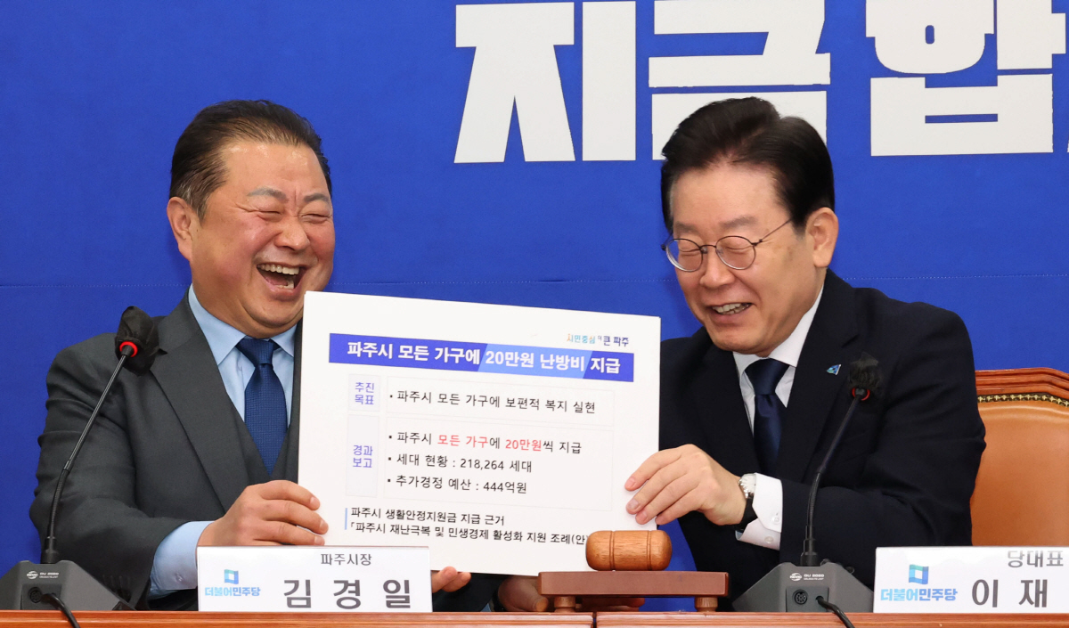 ▲더불어민주당 이재명 대표가 1일 국회에서 열린 최고위원회의에서 김경일 파주시장의 발언 전 ‘파주시 모든 가구에 20만원 난방비 지급’이라고 쓴 피켓을 대신 들어주겠다며 밝게 웃고 있다. (연합뉴스)