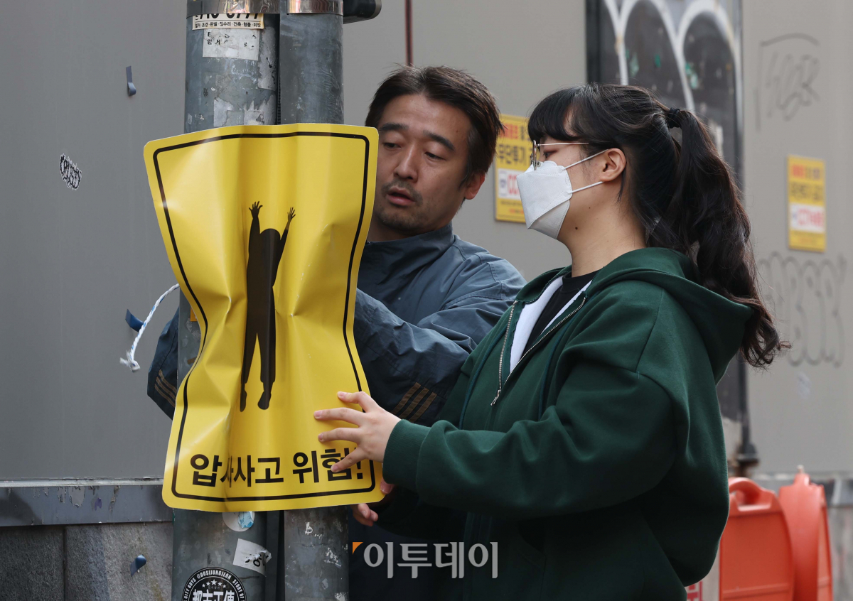 ▲2022년 11월 10일, 홍대 거리에서 이제석 이제석광고연구소 대표와 청년활동가가 연구소가 제작한 압사 사고 위험구간 표지판을 시범 부착하고 있다. 연구소는 좁은 골목 등에서 인파로 인한 압사사고의 위험성을 직관적으로 알리기 위해 표지판을 구겨 표현했다.  (신태현 기자 holjjak@)