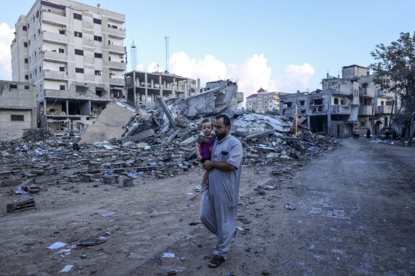 ▲팔레스타인 가자지구 남부 라파 난민촌에서 16일(현지시간) 아버지로 보이는 한 남성이 아이를 안고 이스라엘군 공습으로 폐허가 된 지역을 지나가고 있다. 가자(팔레스타인)/AFP연합뉴스 
