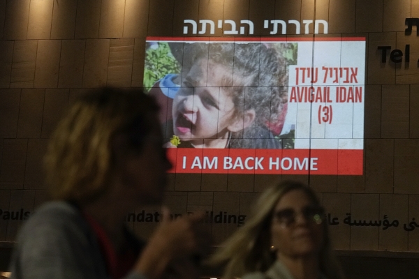 ▲26일(현지시간) 팔레스타인 무장단체 하마스로부터 석방된 미국 국적의 4세 애비게일 이단의 사진 앞앞을 사람들이 스쳐 지나가고 있다. 텔아비브/AP연합뉴스
